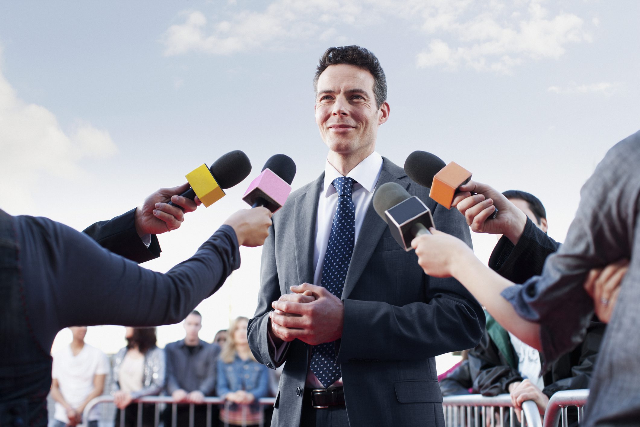 Man in suit speaking to multiple microphones.